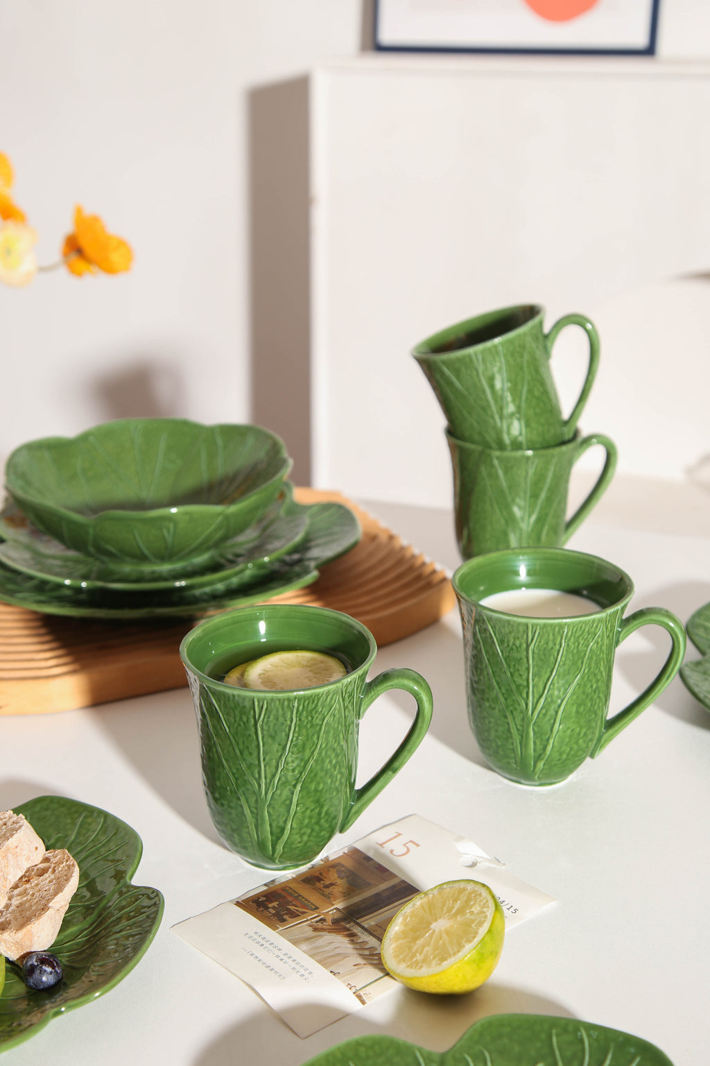 Green ceramic tableware set on a white surface with a lemon and a magazine.